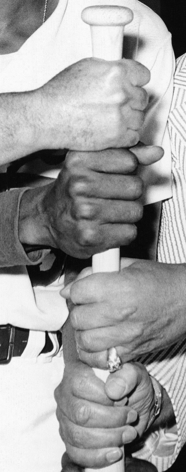 “Four Hands and a Baseball Bat” by John Baldessari, A black and white photo featuring four hands of different skin tones and ages, all grasping a baseball bat together, layered one above the other.