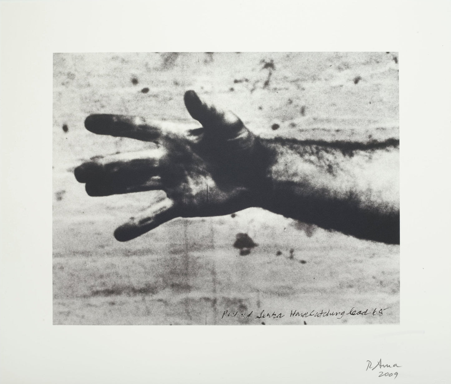 Still from “Hand Catching Lead” by Richard Serra, a print featuring a black-and-white photograph of a muscular arm extended horizontally across the frame from the right side. The hand’s fingers are spread wide, showcasing visible veins and hair, demonstrating strength and tension. There is a textured background, possibly a concrete wall.