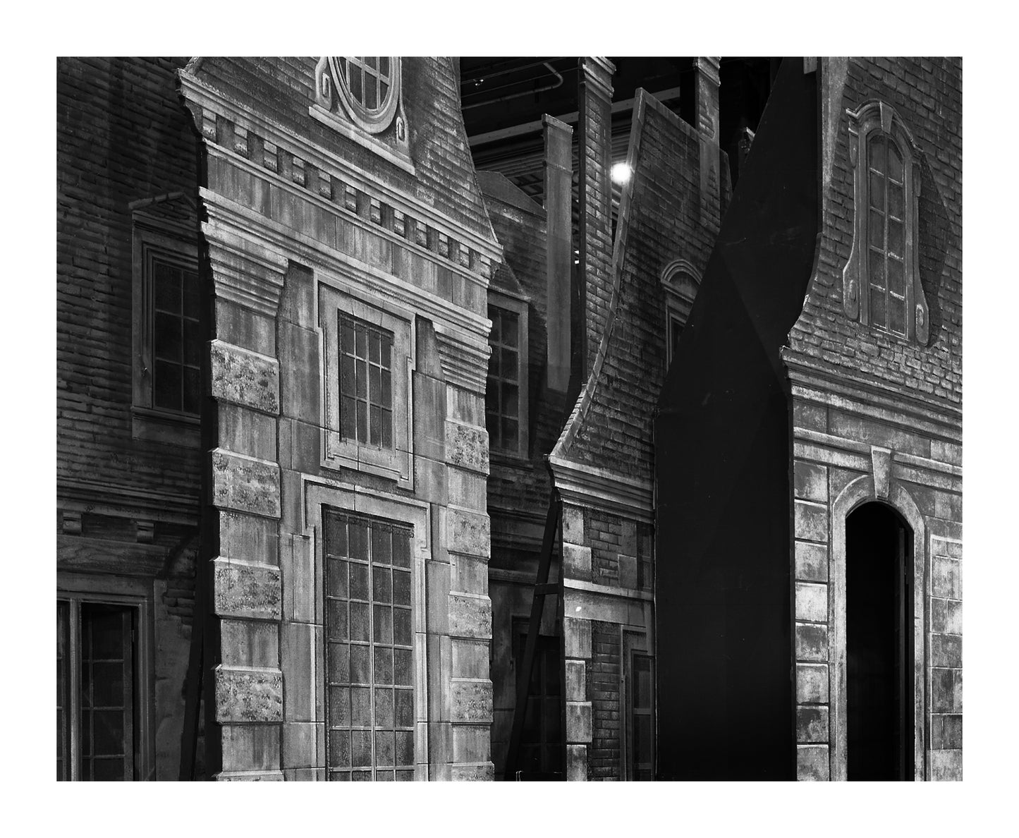 	“Manon Building Façade” by Abelardo Morell, monochromatic architectural composition showcasing an intricate play of light and shadow on a series of ornate façades. The realistic detailing and perspective create a surreal, almost impressionist ambiance.